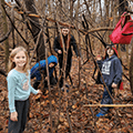 three kids and young adult making a tree fort with long branches