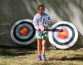 Child holding arrows walking away from two archery targets