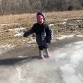 small child in winter clothing standing on a frozen puddle