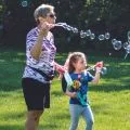 grandmother and granddaughter blowing bubbles in a field