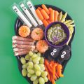 a charcuterie board in the shape of a scull full of halloween themed snacks