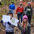 Five people on a wooded trail in fall. Two children in front are holding up turkey puzzles.