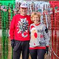 two adults in holiday sweaters standing in front of a colorful backdrop of streamers