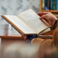 hands holding an open book while sitting at a desk