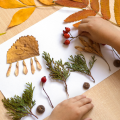 hands placing colorful items from nature onto a piece of paper to make a piece of art