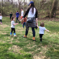 a woman holding hands with two young children as they hike with a group in the woods