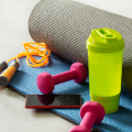 A blue yoga mat rolled up with small pink hand weights an orange jump rope a phone and a green water bottle placed on top