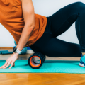 A woman wearing an orange shirt and black pants rolling a foam roller under her hip