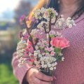 a woman in a pink sweater holding a bouquet of real flowers and lego flowers