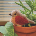 a needle felted bird sitting on a clay pot