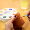 Terracotta pot being painted by someone with a paint palate in the background