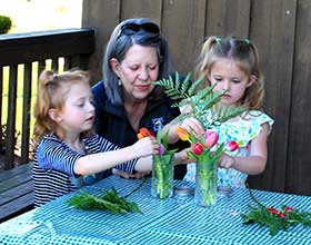 An adult and two children arranging flowers in a vase