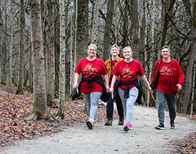 Four people walking along a gravel path. They are wearing matching red t-shirts.