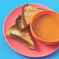 two grilled cheese sandwich halves next to a bowl of tomato soup in an orange bowl