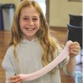 winterslime_120x120 a young girl smiling and holding pink slime stretched between her hands