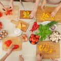 5 pairs of hands working around a table to chop various vegetables on cutting boards