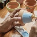 hands painting a terracotta flower pot with blue paint