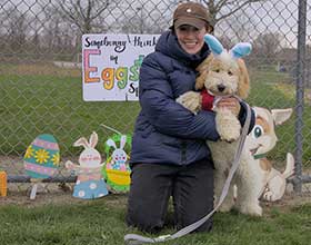 A person hugging a dog in front of a fence and Easter decorations