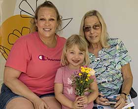 Two adults and a child. Child is holding flowers.