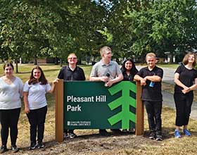 A group of seven people standing behind a green sign that says Pleasant Hill Park.