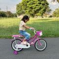 young girl pedaling a pink bike on a paved path