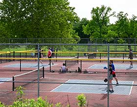 A group of people playing pickleball on outdoor courts.