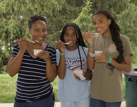 A group of three people smile for the camera while holding ice cream sundaes and spoons up to their mouths.