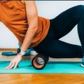 A woman wearing an orange shirt and black pants rolling a foam roller under her hip