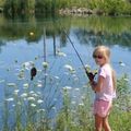 young girl standing by a pond holding a fishing rod with a fish attached