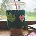 a green felt cup coozie hand sewn with leaves and hearts made out of felt sewn onto it