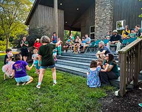 A group of adults and small children sit outside on the steps of the Kennard Nature Nook