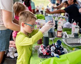 A child is tie-dying at a picnic table in a park shelter
